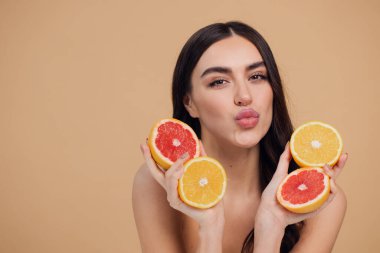 Genç bir kadının portresi, portakal rengi greyfurt gülümseyen dişlerin yarısını beslenen vejetaryen vitamin yaz vitamini, saç bakımı, doğal organik vegan narenciye bej arka planda.