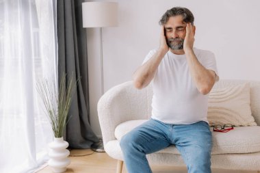 Ev, son sınıf öğrencisi ve stres, duygusal çatışma ve geçici baş dönmesi için kanepede baş ağrısı. Oturma odası, kanepe ve evde emeklilikten doğan acı, migren ve endişe içinde yaşlı bir adam.