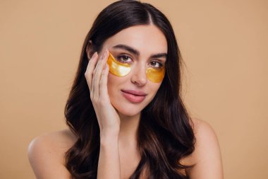 Saf, güzel, kibar bir kadının güzel görüntüsü. Çıplak, soyutlanmış bir kamera gibi duruyor. Bej arka planda altın rengi bantlarla cildine dikkat et.