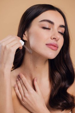 Bej arka planda Serum Bırakan Kadın. Pipette 'ten Serum Kolajeni Nemlendirici kullanan Avrupalı Kız. Yakın plan. Pozitif Gülen Güzel Kadın Portresi. Yüz Cildi Bakımı Konsepti