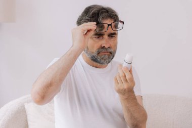 Gözlüklü kıdemli adam evde ilaç tarifini ve talimatlarını okur. Kişisel bakım konsepti, yaşlılar, kopyalama alanı.