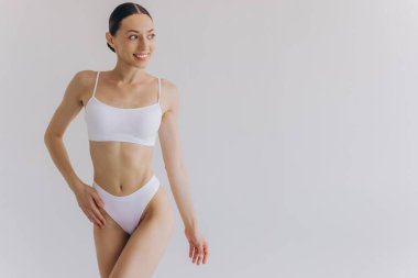 Manzarayı kapat. Zayıf vücutlu güzel bir kadın ve beyaz stüdyo arka planında iç çamaşırlarıyla poz veren mükemmel bir karın..