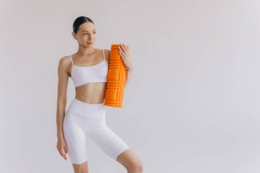 Beyaz spor giysili güzel, ince kadın spor kıyafetleri içinde, spor salonu için turuncu köpük silindirli, fotokopi alanlı beyaz poz veren, sağlığını ve sağlığını destekleyen,.