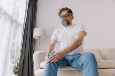 Ev, diz ağrısı ve koltukta eklem iltihabı, kemik erimesi ve fibromiyalji olan yaşlı bir adam. Rahatlama, kas gerilimi ve kaza ya da emeklilikte yaralanma için eklem masajı yapan yaşlı erkek.