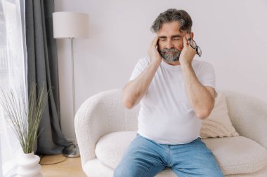 Ev, son sınıf öğrencisi ve stres, duygusal çatışma ve geçici baş dönmesi için kanepede baş ağrısı. Oturma odası, kanepe ve evde emeklilikten doğan acı, migren ve endişe içinde yaşlı bir adam.