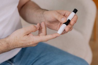 Tekerlekli sandalyedeki diyabetik kıdemli adam kan şekeri seviyesini parmak ölçer, glikoz ölçer. Tip 1 diyabeti olan yaşlı bir adam evde kan şekeri monitörü kullanıyor..