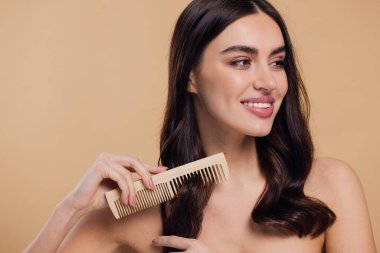 Çıplak omuzlarını bayanla su kuyusu-damat rüya gibi esmer saç o ahşap fırça pastel bej renkli arka plan üzerinde izole ile saç tarama büyüleyici portre yapmak beyaz ışınlama dişleri kazma dişli bir gülümseme