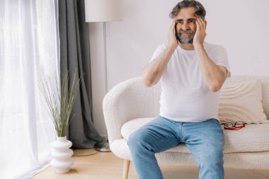 Ev, son sınıf öğrencisi ve stres, duygusal çatışma ve geçici baş dönmesi için kanepede baş ağrısı. Oturma odası, kanepe ve evde emeklilikten doğan acı, migren ve endişe içinde yaşlı bir adam.