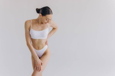 Manzarayı kapat. Zayıf vücutlu güzel bir kadın ve beyaz stüdyo arka planında iç çamaşırlarıyla poz veren mükemmel bir karın..