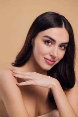 Güzel, genç, esmer, bej arkaplan, yüz bakımı, kozmetik, güzellik ve kaplıca, gülümseyen kadın portresi.