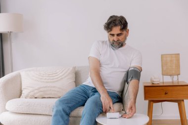 Evdeki kanepede oturmuş, tansiyonunu ölçen, gri saçlı, son sınıf öğrencisi. Modern tonometre kullanan emekli, hipertansiyon deneyimi yaşayan, kopyalama alanı