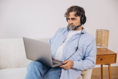 Dedem dizüstü bilgisayar ve kulaklık kullanıyormuş. Koltukta oturuyormuş. Evden çalışan kıdemli adam, çevrimiçi toplantı, görüntülü konuşma, kopyalama alanı