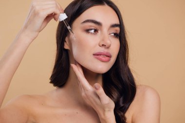 Bej arka planda Serum Bırakan Kadın. Pipette 'ten Serum Kolajeni Nemlendirici kullanan Avrupalı Kız. Yakın plan. Pozitif Gülen Güzel Kadın Portresi. Yüz Cildi Bakımı Konsepti