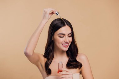 Bej arka planda saç köklerine gerekli yağı uygulayan mutlu genç kadının güzel portresi, metin için boşluk