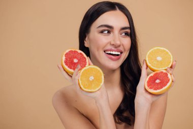 Genç bir kadının portresi, portakal rengi greyfurt gülümseyen dişlerin yarısını beslenen vejetaryen vitamin yaz vitamini, saç bakımı, doğal organik vegan narenciye bej arka planda.