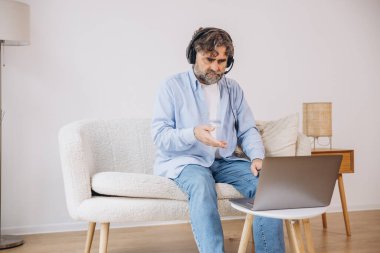 Dedem dizüstü bilgisayar ve kulaklık kullanıyormuş. Koltukta oturuyormuş. Evden çalışan kıdemli adam, çevrimiçi toplantı, görüntülü konuşma, kopyalama alanı