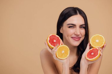 Genç bir kadının portresi, portakal rengi greyfurt gülümseyen dişlerin yarısını beslenen vejetaryen vitamin yaz vitamini, saç bakımı, doğal organik vegan narenciye bej arka planda.