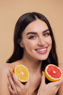 Genç bir kadının portresi, portakal rengi greyfurt gülümseyen dişlerin yarısını beslenen vejetaryen vitamin yaz vitamini, saç bakımı, doğal organik vegan narenciye bej arka planda.