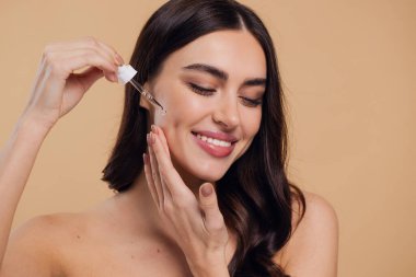 Bej arka planda Serum Bırakan Kadın. Pipette 'ten Serum Kolajeni Nemlendirici kullanan Avrupalı Kız. Yakın plan. Pozitif Gülen Güzel Kadın Portresi. Yüz Cildi Bakımı Konsepti