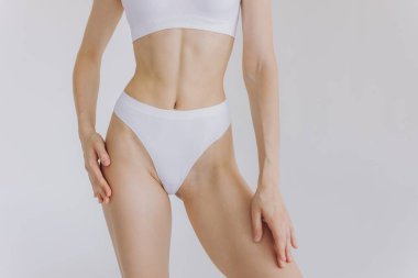 Beyaz arka planda izole edilmiş iç çamaşırlı, tanınmayan fit bir kadını yakından çek. Düz göbekli, beyaz iç çamaşırlı, zayıf, çekici bir kadın gövdesi. Metin için alanı kopyala.