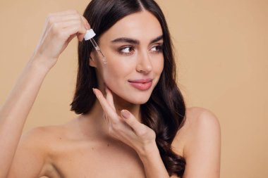 Bej arka planda Serum Bırakan Kadın. Pipette 'ten Serum Kolajeni Nemlendirici kullanan Avrupalı Kız. Yakın plan. Pozitif Gülen Güzel Kadın Portresi. Yüz Cildi Bakımı Konsepti