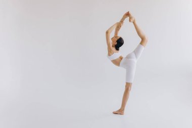 Zayıf vücutlu, beyaz arka planda izole yoga yapan sportif genç bir kadın. Vücut ve zihinsel gelişim arasındaki sağlıklı yaşam ve doğal denge kavramı.