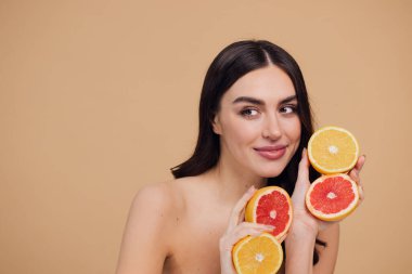 Genç bir kadının portresi, portakal rengi greyfurt gülümseyen dişlerin yarısını beslenen vejetaryen vitamin yaz vitamini, saç bakımı, doğal organik vegan narenciye bej arka planda.