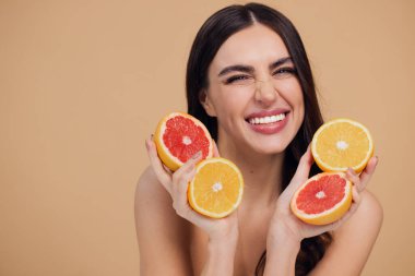 Genç bir kadının portresi, portakal rengi greyfurt gülümseyen dişlerin yarısını beslenen vejetaryen vitamin yaz vitamini, saç bakımı, doğal organik vegan narenciye bej arka planda.