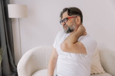 Üst sınıflardan biri içeride oturuyor, boynu ağrıyormuş gibi görünüyor. Üzüntülü bir ifadeyle boynunu tutuyor, rahatsız olduğunu gösteriyor..