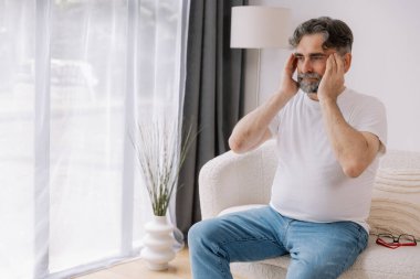 Ev, son sınıf öğrencisi ve stres, duygusal çatışma ve geçici baş dönmesi için kanepede baş ağrısı. Oturma odası, kanepe ve evde emeklilikten doğan acı, migren ve endişe içinde yaşlı bir adam.