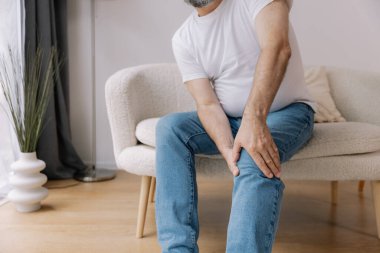Ev, diz ağrısı ve koltukta eklem iltihabı, kemik erimesi ve fibromiyalji olan yaşlı bir adam. Rahatlama, kas gerilimi ve kaza ya da emeklilikte yaralanma için eklem masajı yapan yaşlı erkek.