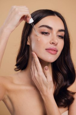 Bej arka planda Serum Bırakan Kadın. Pipette 'ten Serum Kolajeni Nemlendirici kullanan Avrupalı Kız. Yakın plan. Pozitif Gülen Güzel Kadın Portresi. Yüz Cildi Bakımı Konsepti