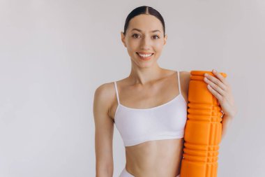 Beyaz spor giysili güzel, ince kadın spor kıyafetleri içinde, spor salonu için turuncu köpük silindirli, fotokopi alanlı beyaz poz veren, sağlığını ve sağlığını destekleyen,.