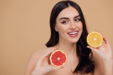 Genç bir kadının portresi, portakal rengi greyfurt gülümseyen dişlerin yarısını beslenen vejetaryen vitamin yaz vitamini, saç bakımı, doğal organik vegan narenciye bej arka planda.