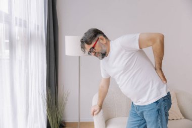 Hasta, mutsuz, yaşlı bir adam, kas hasarına dokunuyor. Sırtında ağrılar var. Evde sırt ağrısı. Fiziksel yaralanma ve sağlık sorunları