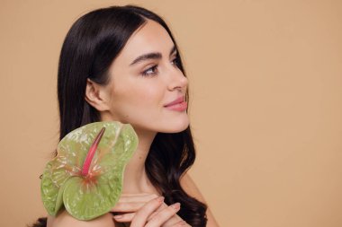 Bej renkli stüdyo arka planında izole edilmiş çiçekle poz veren çekici genç bir kadının güzel portresi.