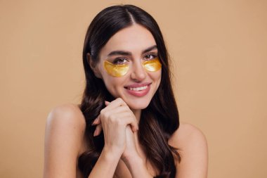 Saf, güzel, kibar bir kadının güzel görüntüsü. Çıplak, soyutlanmış bir kamera gibi duruyor. Bej arka planda altın rengi bantlarla cildine dikkat et.