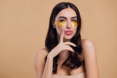 Saf, güzel, kibar bir kadının güzel görüntüsü. Çıplak, soyutlanmış bir kamera gibi duruyor. Bej arka planda altın rengi bantlarla cildine dikkat et.