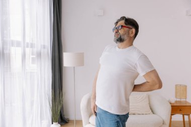 Hasta, mutsuz, yaşlı bir adam, kas hasarına dokunuyor. Sırtında ağrılar var. Evde sırt ağrısı. Fiziksel yaralanma ve sağlık sorunları