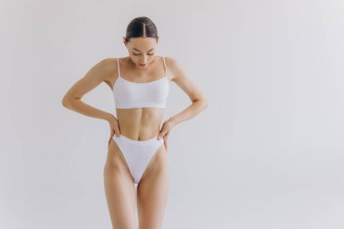 Manzarayı kapat. Zayıf vücutlu güzel bir kadın ve beyaz stüdyo arka planında iç çamaşırlarıyla poz veren mükemmel bir karın..