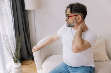 Üst sınıflardan biri içeride oturuyor, boynu ağrıyormuş gibi görünüyor. Üzüntülü bir ifadeyle boynunu tutuyor, rahatsız olduğunu gösteriyor..