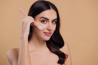 Yarı çıplak kadın, güzellik için yüz ve fırça kremi, kuaför ve cilt bakımı bej arka planda. Mutlu model, yüz losyonu ve dermatoloji, kolajen ve mutluluğun gülümsemesi için makyaj malzemesi.