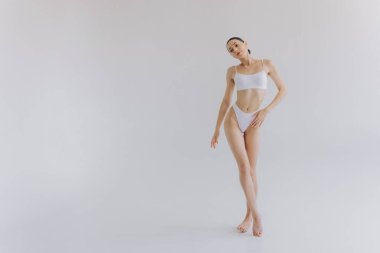 İnce vücutlu, beyaz stüdyo arka planında fotokopi aletiyle poz veren güzel bir kadının tam boy portresi.