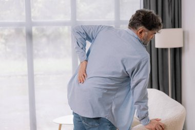 Evdeki kanepede sırt ağrısı çeken yaşlı bir adamın arka görüntüsü, reklamınız için yer açın.