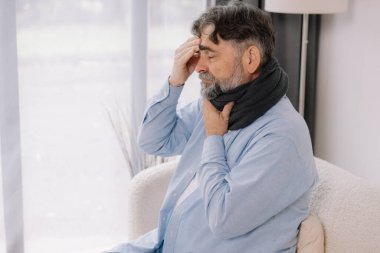 Boğazında anjin olan yaşlı bir adam oturma odasında kanepede otururken elini başına dayayıp grip olmuş.