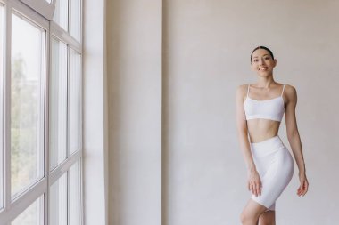 Zayıf vücutlu sportif genç bir kadın, panoramik pencereli modern odada yoga pratiği yapıyor. Vücut ve zihinsel gelişim arasındaki sağlıklı yaşam ve doğal denge kavramı.