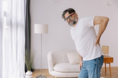 Hasta, mutsuz, yaşlı bir adam, kas hasarına dokunuyor. Sırtında ağrılar var. Evde sırt ağrısı. Fiziksel yaralanma ve sağlık sorunları