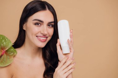 Yeşil çiçeğin yanındaki çekici bir kadının portresi sorun için yüz kremi sürüyor. Bej arka planda merhem var. Refah konsepti