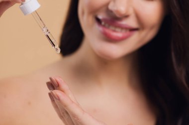 Bej arka planda Serum Bırakan Kadın. Pipette 'ten Serum Kolajeni Nemlendirici kullanan Avrupalı Kız. Yakın plan. Pozitif Gülen Güzel Kadın Portresi. Yüz Cildi Bakımı Konsepti