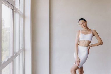 Zayıf vücutlu sportif genç bir kadın, panoramik pencereli modern odada yoga pratiği yapıyor. Vücut ve zihinsel gelişim arasındaki sağlıklı yaşam ve doğal denge kavramı.